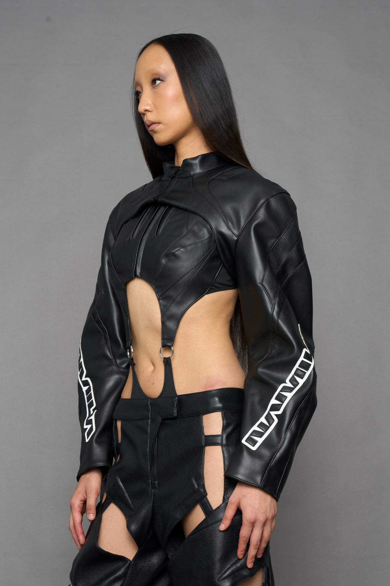 A model wearing a black faux-leather jacket with logo on the arm