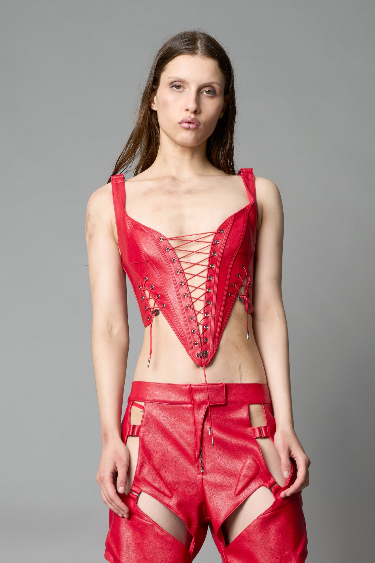 Model wearing red vegan leather XTC Corset by Namilia featuring extreme plunging neckline, front lace-up closure, and sculpted fit
