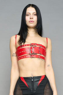 red vegan leather belt top with three adjustable grommet straps, oversized metal buckles, and circular hardware – edgy bondage-inspired crop top for festival or clubwear.
