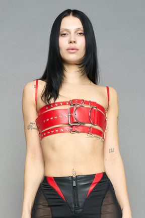 red vegan leather belt top with three adjustable grommet straps, oversized metal buckles, and circular hardware – edgy bondage-inspired crop top for festival or clubwear.

