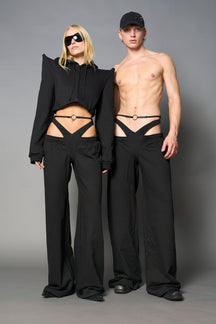 Model wearing low-rise black wide-leg pants featuring a V-shaped waistband and detachable thong strap detail.