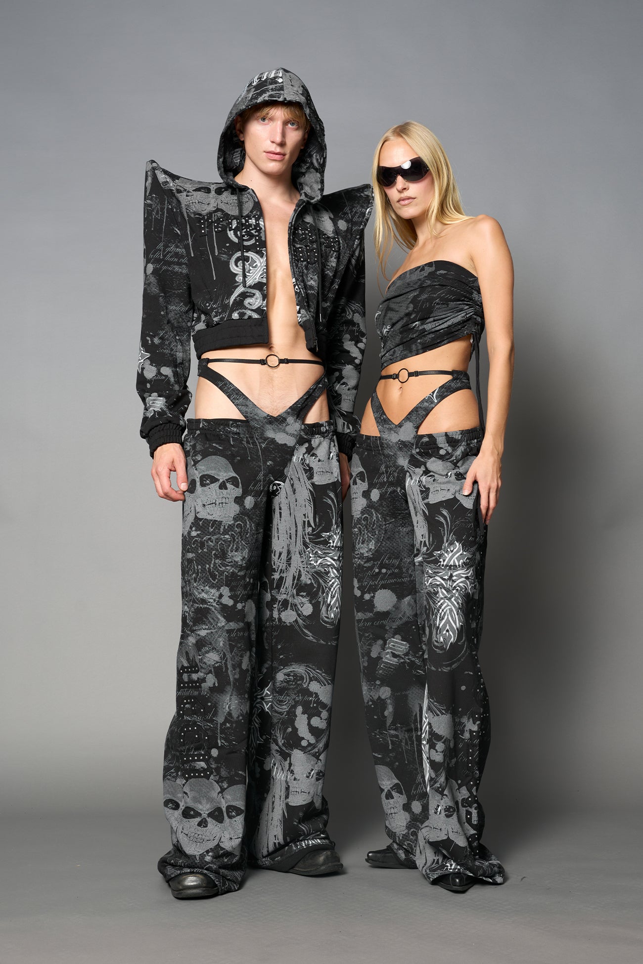 Model wearing low-rise black print wide-leg pants featuring a V-shaped waistband and detachable thong strap detail.