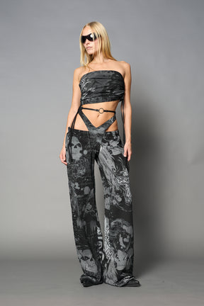 Model wearing low-rise black print wide-leg pants featuring a V-shaped waistband and detachable thong strap detail.