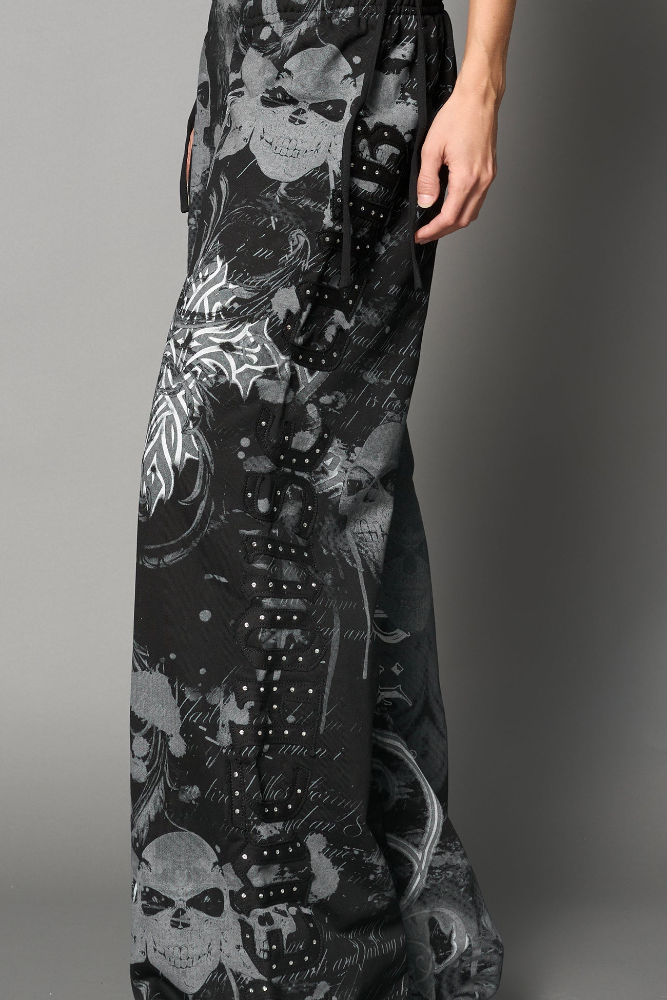 Model wearing low-rise black print wide-leg pants featuring a V-shaped waistband and detachable thong strap detail.