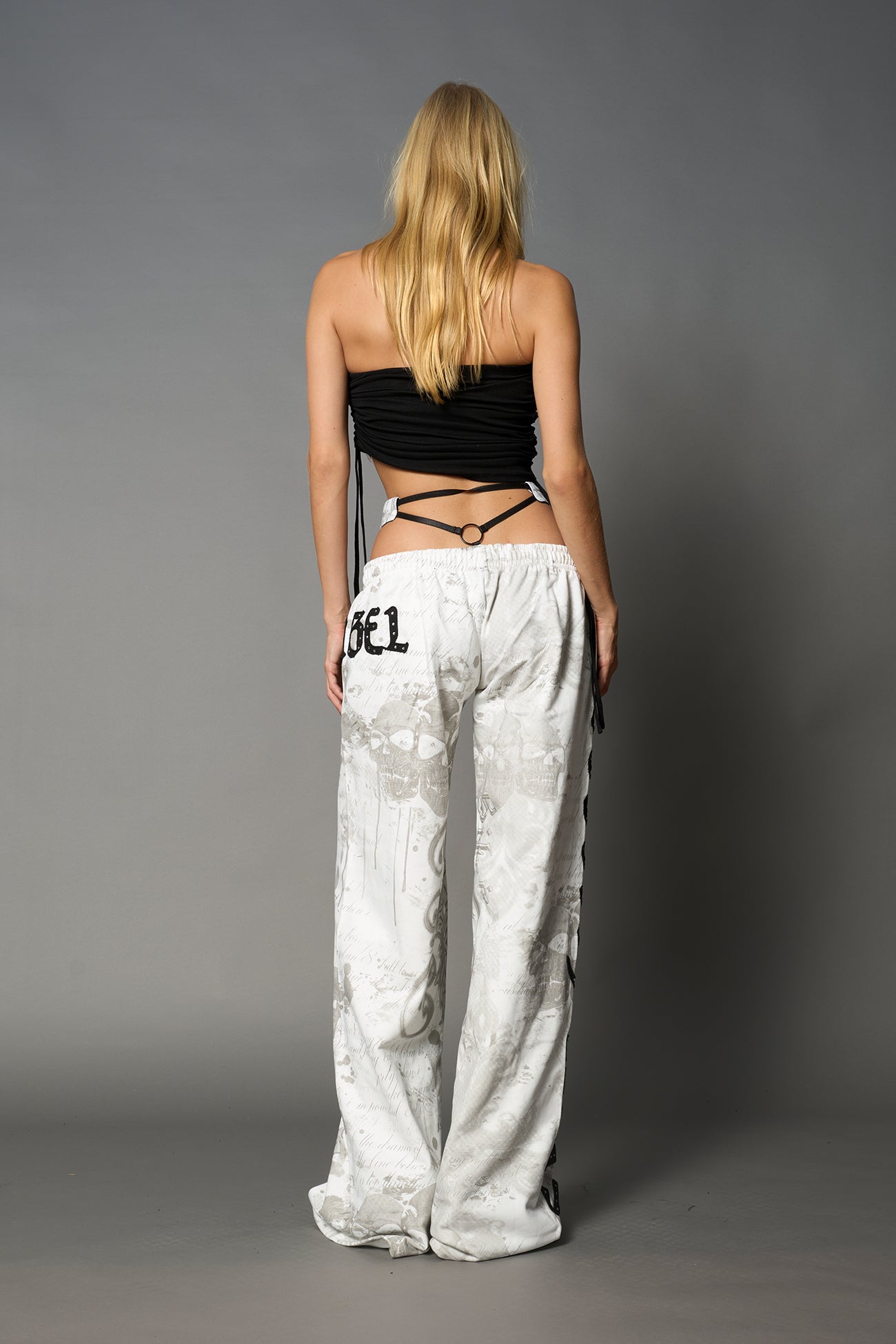 Model wearing low-rise white print wide-leg pants featuring a V-shaped waistband and detachable thong strap detail.
