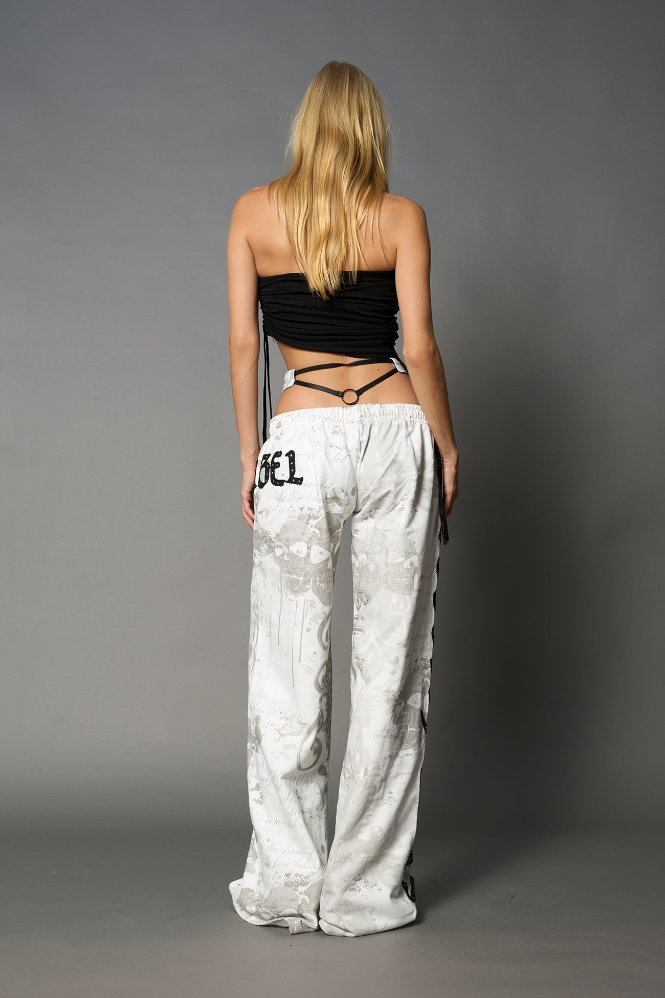 Model wearing low-rise white print wide-leg pants featuring a V-shaped waistband and detachable thong strap detail.