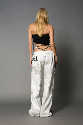 Model wearing low-rise white print wide-leg pants featuring a V-shaped waistband and detachable thong strap detail.