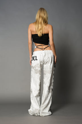 Model wearing low-rise white print wide-leg pants featuring a V-shaped waistband and detachable thong strap detail.