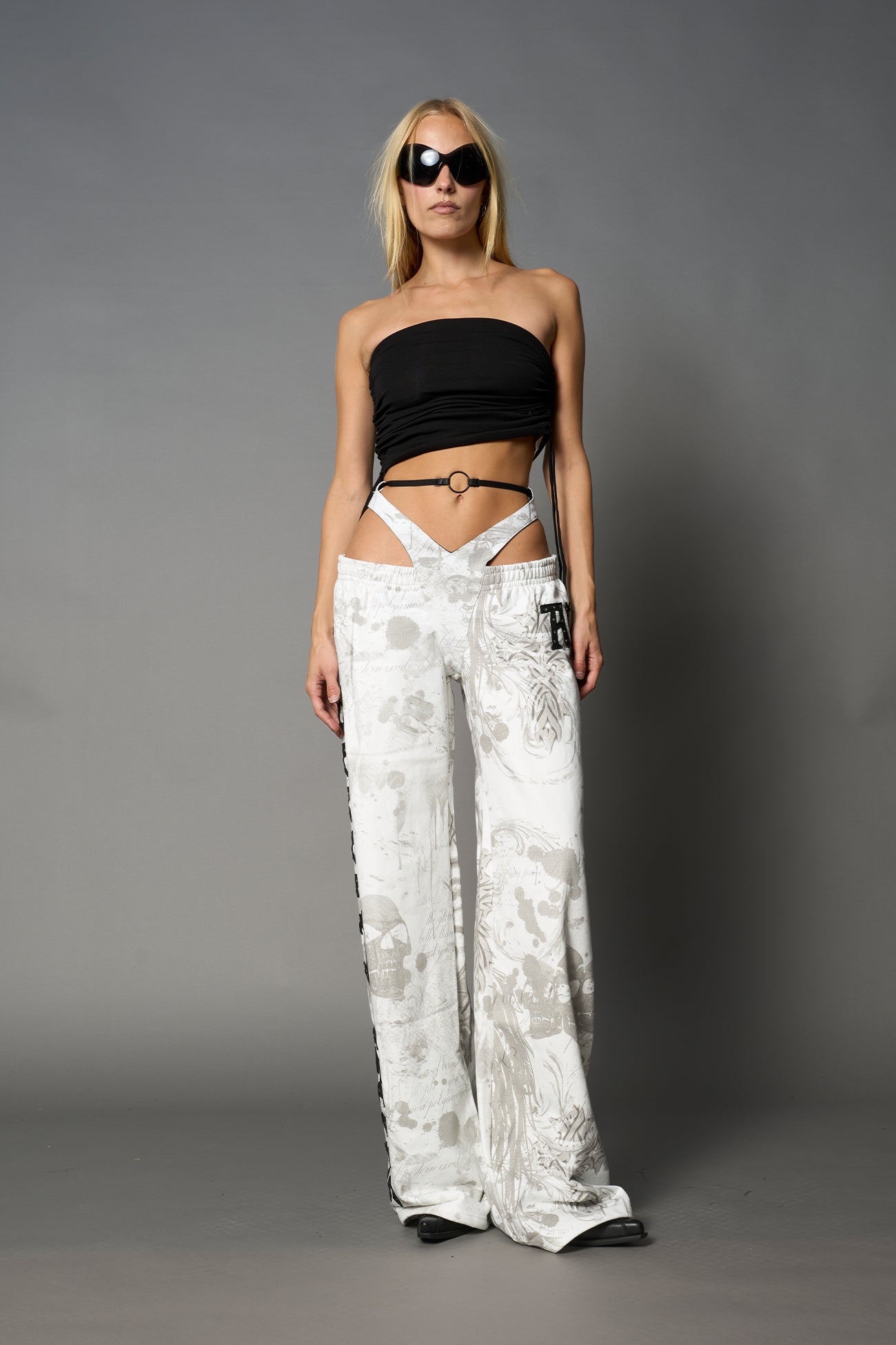 Model wearing low-rise white print wide-leg pants featuring a V-shaped waistband and detachable thong strap detail.