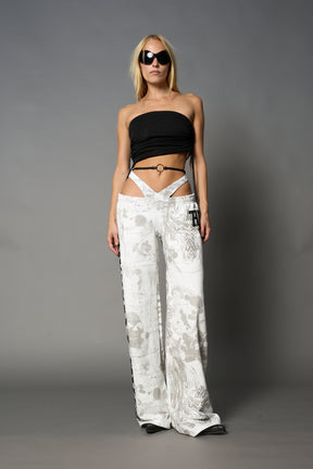 Model wearing low-rise white print wide-leg pants featuring a V-shaped waistband and detachable thong strap detail.
