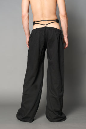Model wearing low-rise black wide-leg pants featuring a V-shaped waistband and detachable thong strap detail.