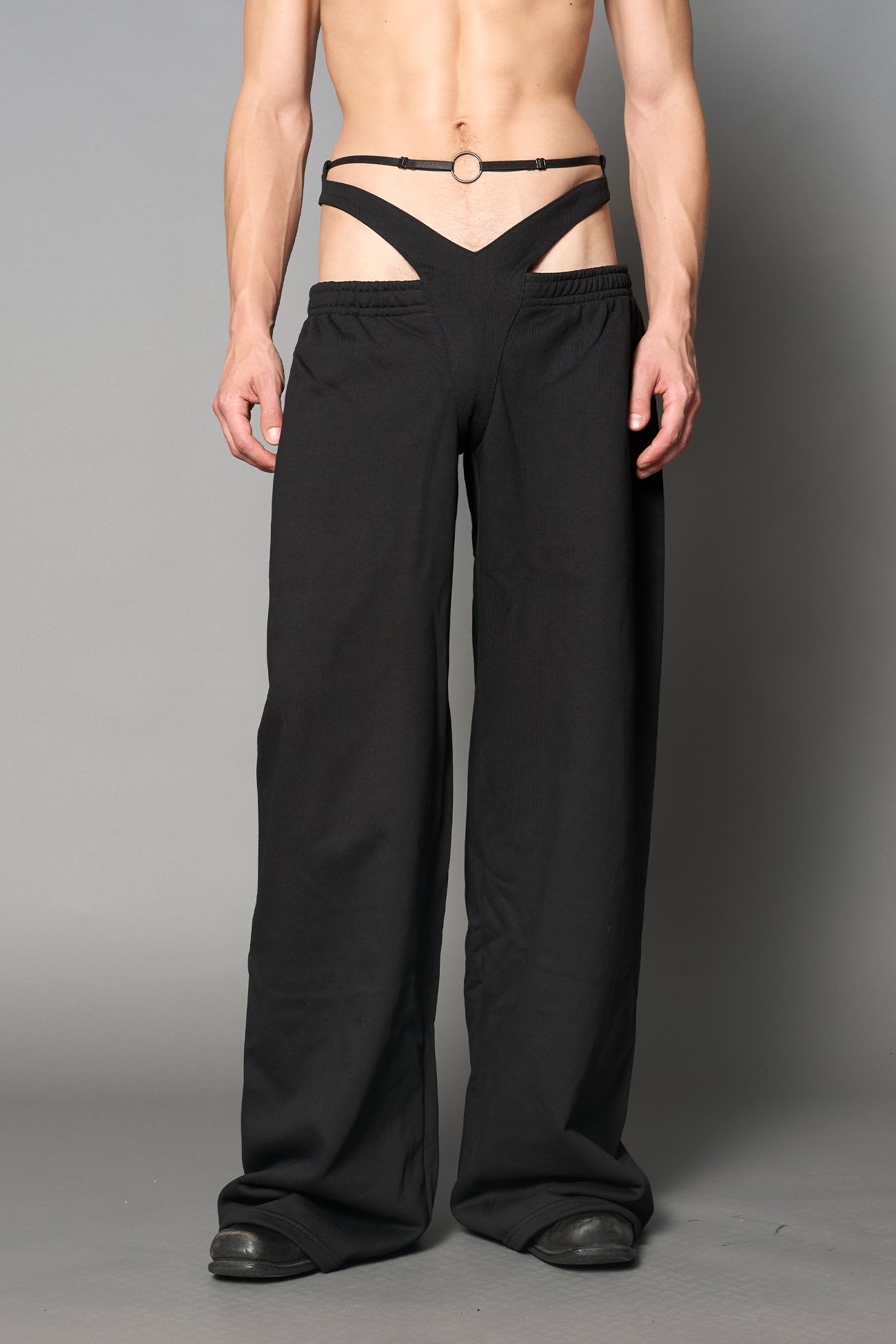Model wearing low-rise black wide-leg pants featuring a V-shaped waistband and detachable thong strap detail.