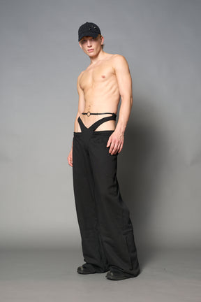Model wearing low-rise black wide-leg pants featuring a V-shaped waistband and detachable thong strap detail.