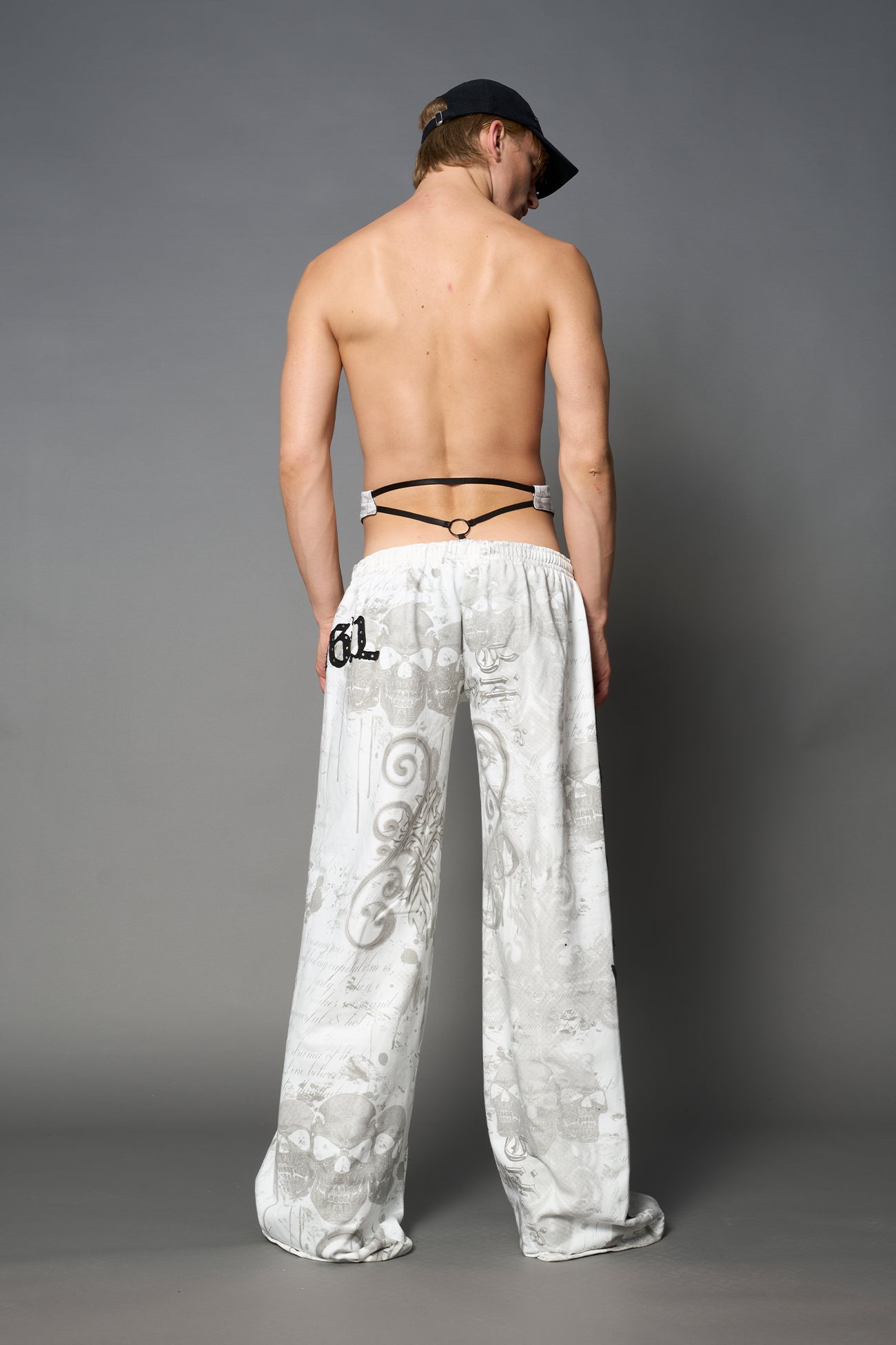 Model wearing low-rise white print wide-leg pants featuring a V-shaped waistband and detachable thong strap detail.