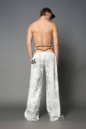 Model wearing low-rise white print wide-leg pants featuring a V-shaped waistband and detachable thong strap detail.