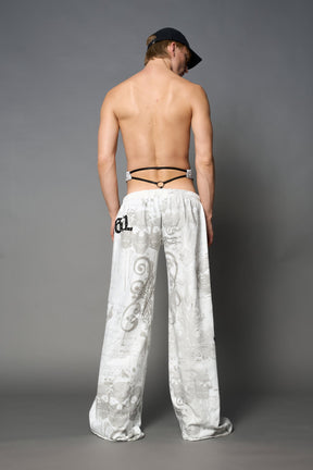 Model wearing low-rise white print wide-leg pants featuring a V-shaped waistband and detachable thong strap detail.