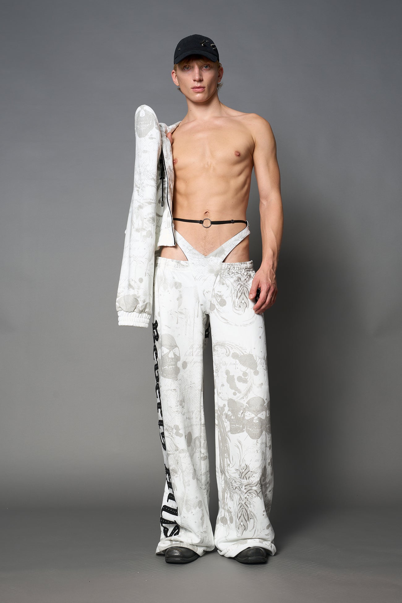 Model wearing low-rise white print wide-leg pants featuring a V-shaped waistband and detachable thong strap detail.