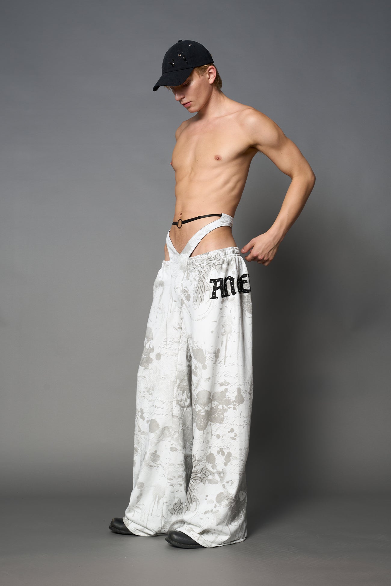 Model wearing low-rise white print wide-leg pants featuring a V-shaped waistband and detachable thong strap detail.
