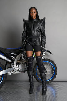 Model wears the black Namilia Spike Moto Jacket with wire shoulder pads, branded zipper, band collar, zippered breast and waist pockets, motocross-style lines, and black logo rubber tag on the back.