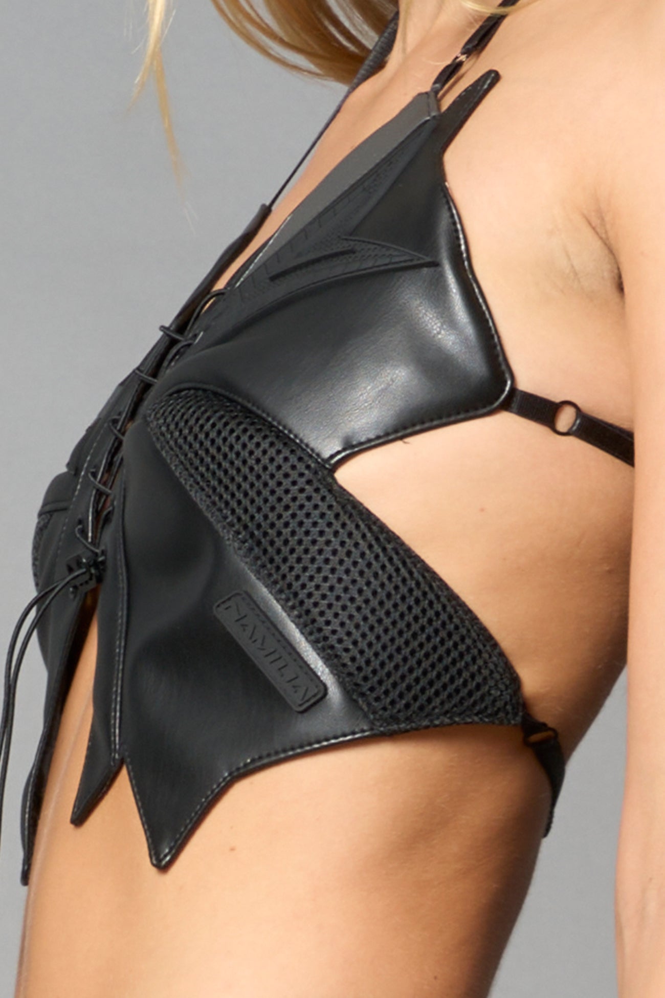 model wears black vegan leather butterfly crop top with lace-up front, halter straps, and mesh accents – edgy Y2K-inspired statement piece for festivals or streetwear.