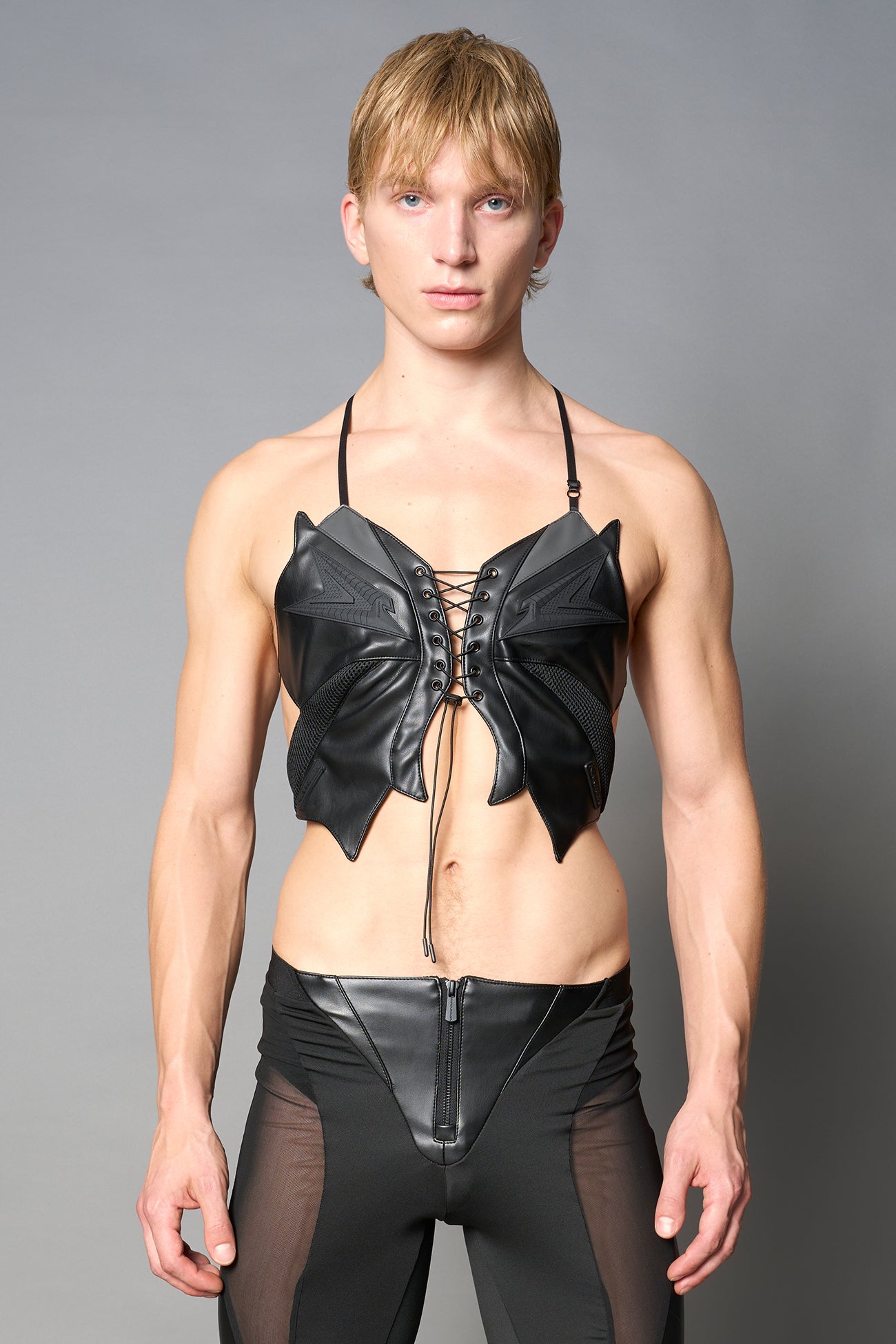 model wears black vegan leather butterfly crop top with lace-up front, halter straps, and mesh accents – edgy Y2K-inspired statement piece for festivals or streetwear.