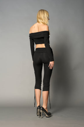Model wearing black capri pants with ruched sides and matching off-shoulder crop top