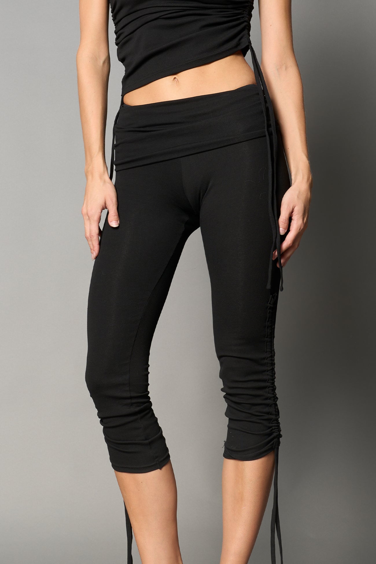 Model wearing black capri pants with ruched sides and matching off-shoulder crop top