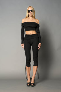 Model wearing black capri pants with ruched sides and matching off-shoulder crop top