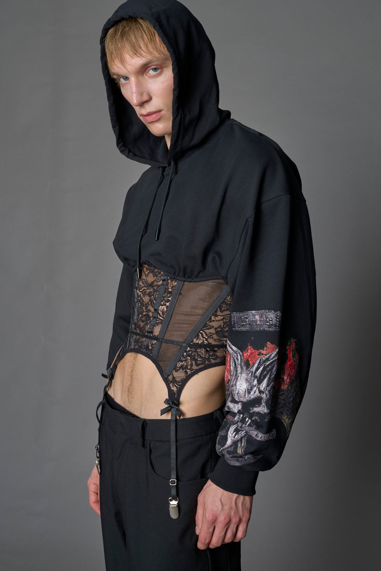 male model wearing a lingerie-inspired black hoodie with a lace corset and a goth-inspired print