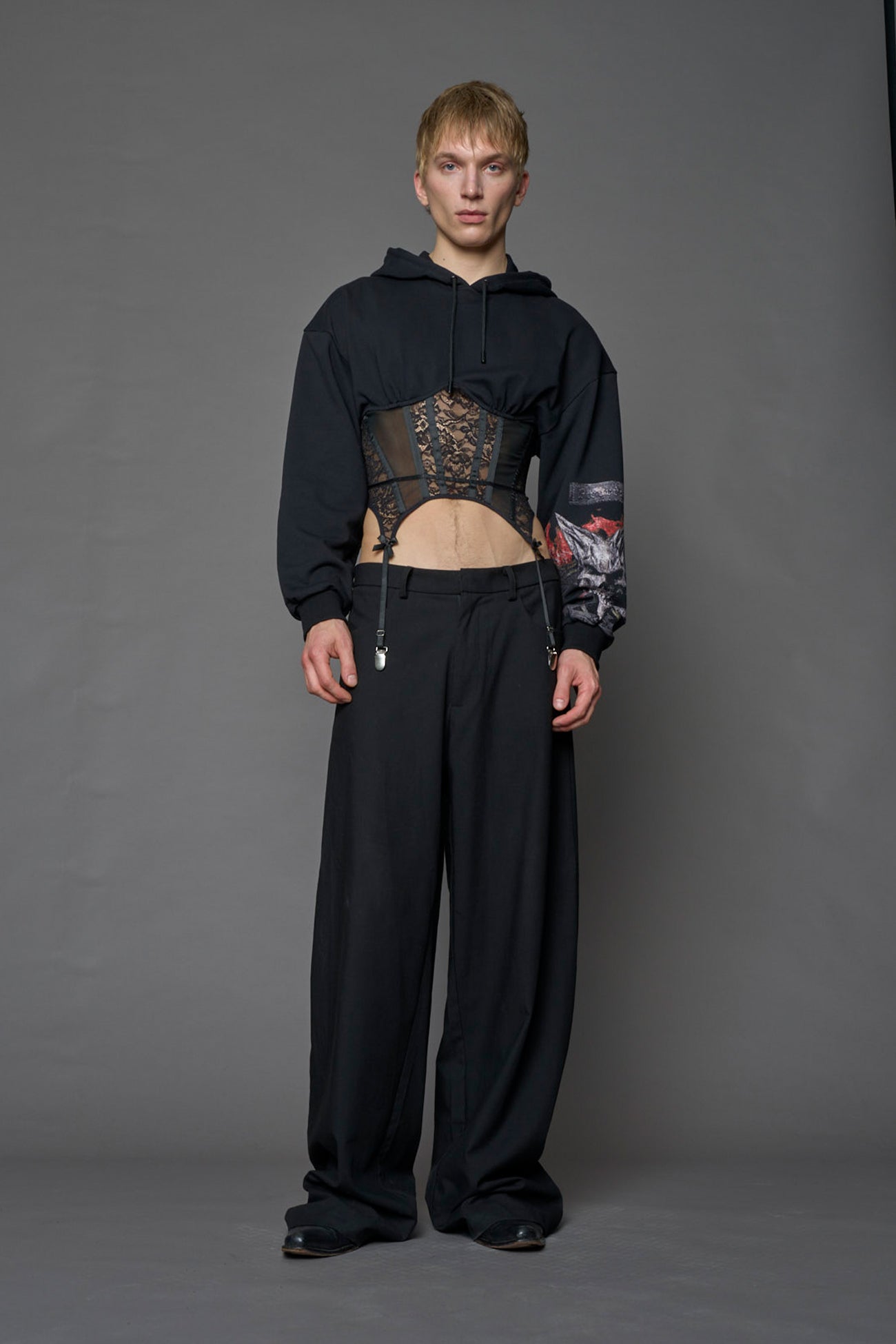 male model wearing a lingerie-inspired black hoodie with a lace corset and a goth-inspired print