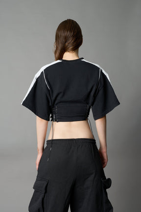 Front view of model in washed-black Namilia Corset-T shirt with sculpted corset-style waist, curved hemline, and oversized sleeves