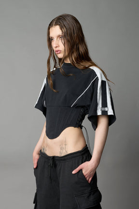 Front view of model in washed-black Namilia Corset-T shirt with sculpted corset-style waist, curved hemline, and oversized sleeves