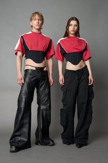 Front view of model in red Namilia Corset-T shirt with sculpted corset-style waist, curved hemline, and oversized sleeves, styled with leather mini skirt and moto boots.