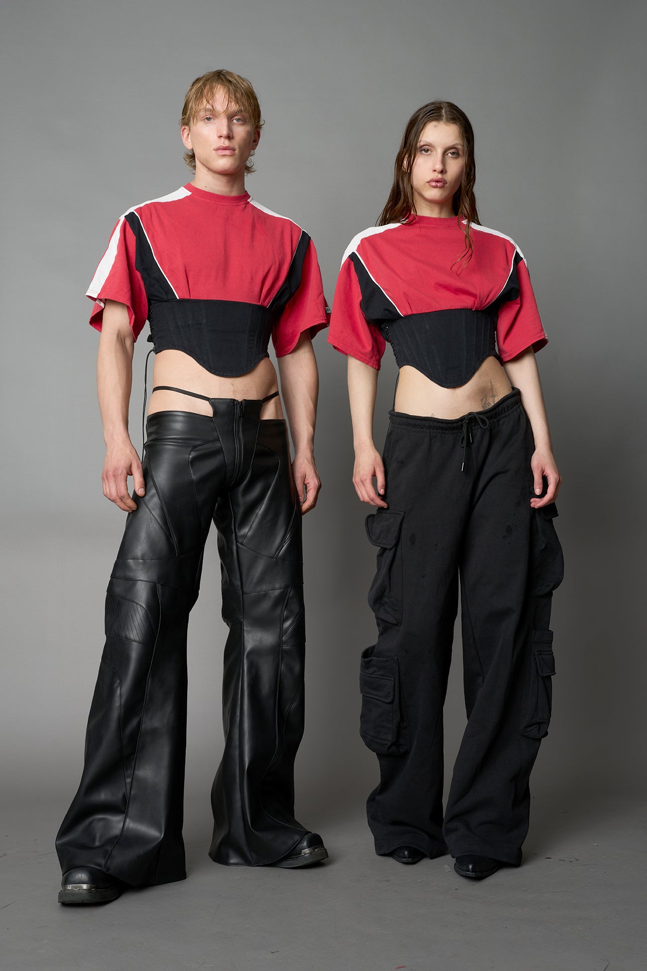 Front view of model in red Namilia Corset-T shirt with sculpted corset-style waist, curved hemline, and oversized sleeves, styled with leather mini skirt and moto boots.