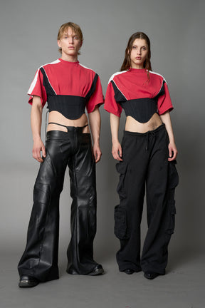 Front view of model in red Namilia Corset-T shirt with sculpted corset-style waist, curved hemline, and oversized sleeves, styled with leather mini skirt and moto boots.