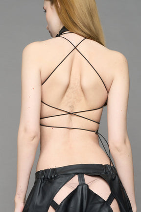 Black coated denim biker top by NAMILIA with high neck zip front, sculpted corset-style seams, open sides with string lacing, and criss-cross open back, worn by model on neutral background.