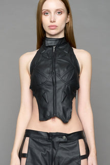 Black coated denim biker top by NAMILIA with high neck zip front, sculpted corset-style seams, open sides with string lacing, and criss-cross open back, worn by model on neutral background.