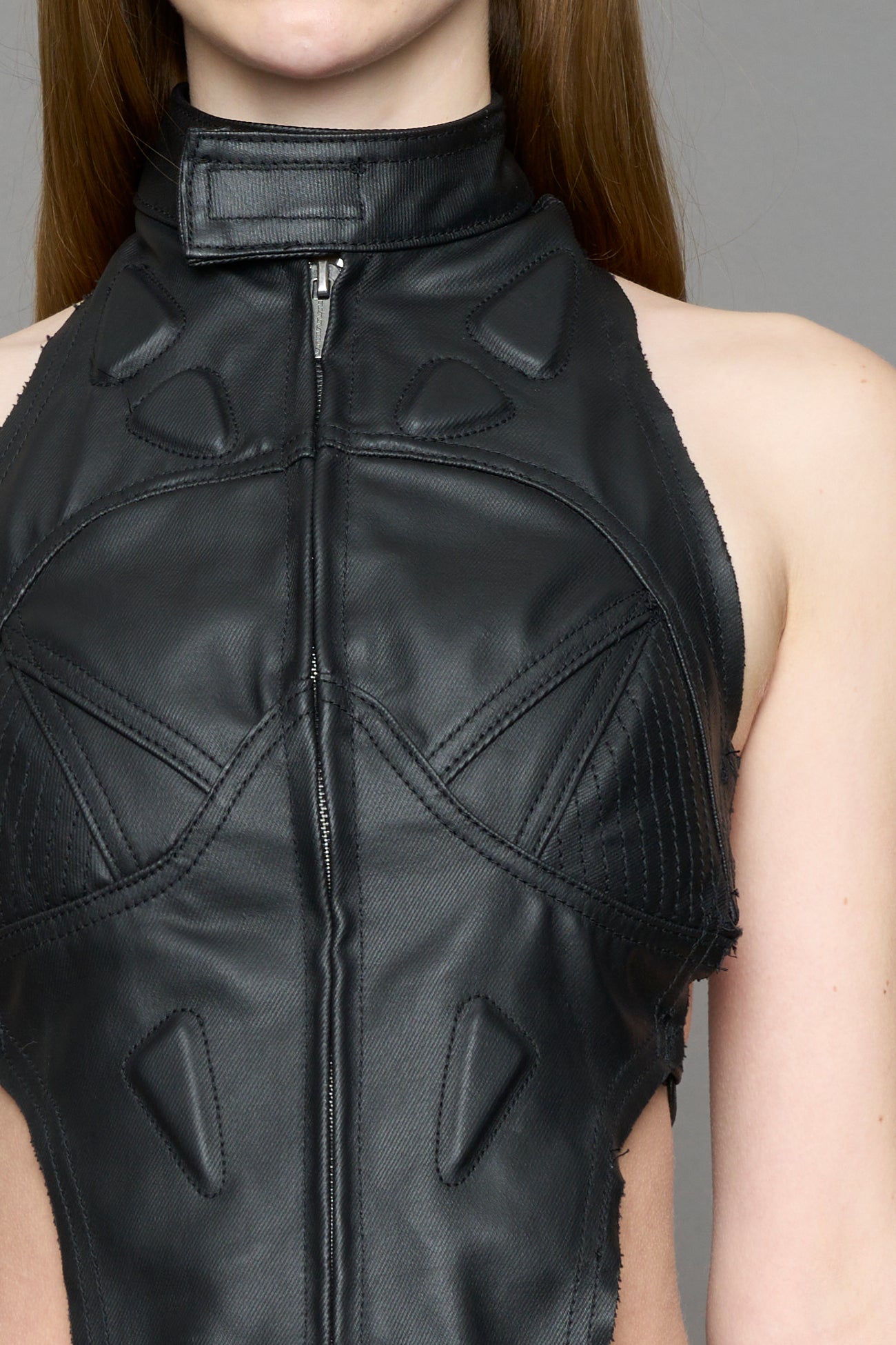 Black coated denim biker top by NAMILIA with high neck zip front, sculpted corset-style seams, open sides with string lacing, and criss-cross open back, worn by model on neutral background.