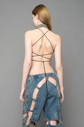 Blue mud denim biker top by NAMILIA with high neck zip front, sculpted corset-style seams, open sides with string lacing, and criss-cross open back, worn by model on neutral background.
