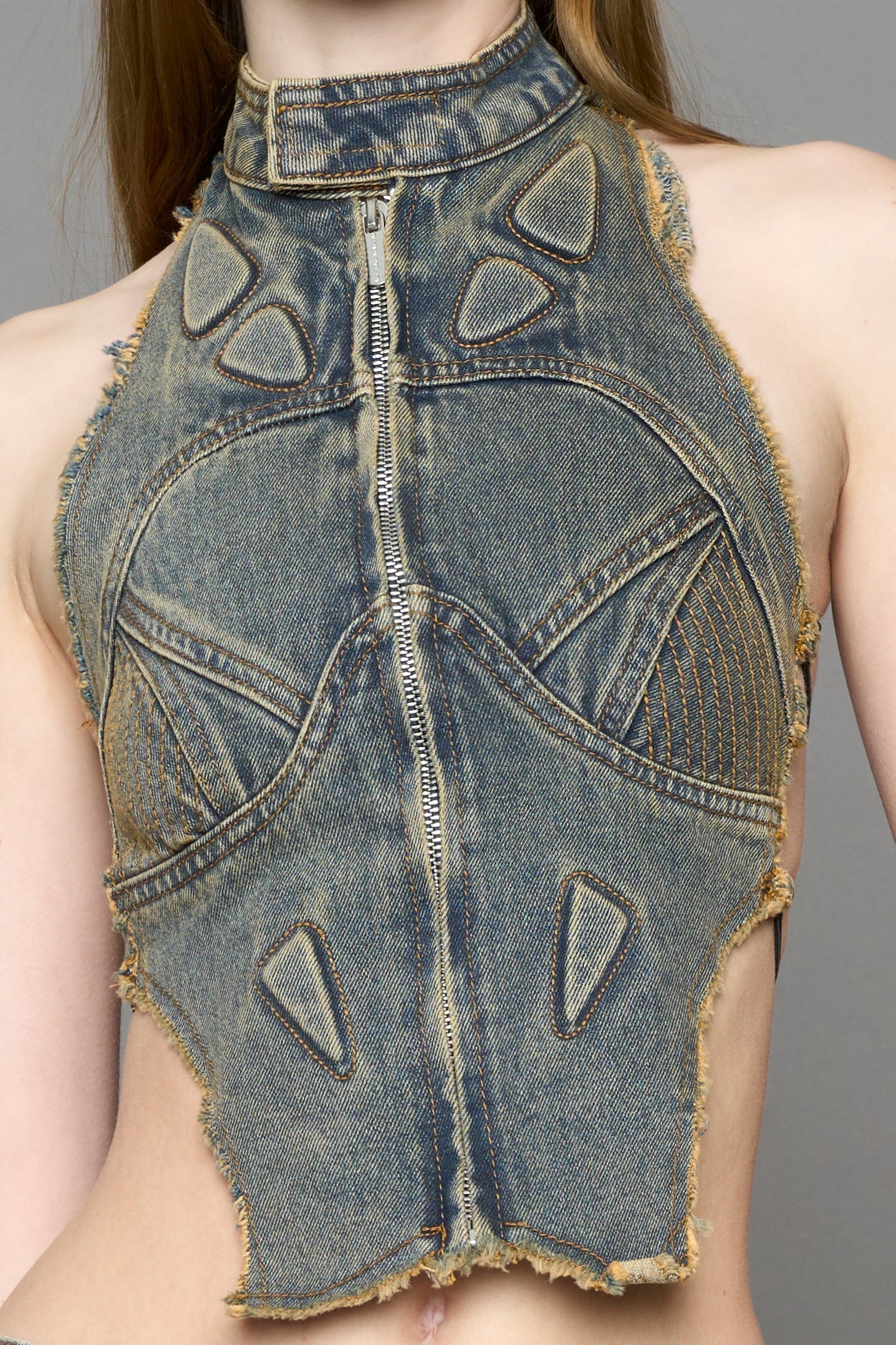 Blue mud denim biker top by NAMILIA with high neck zip front, sculpted corset-style seams, open sides with string lacing, and criss-cross open back, worn by model on neutral background.