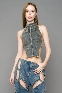 Blue mud denim biker top by NAMILIA with high neck zip front, sculpted corset-style seams, open sides with string lacing, and criss-cross open back, worn by model on neutral background.