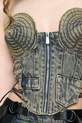 blue mud washed denim cone corset by NAMILIA with spiral-stitched cone cups, strapless fitted silhouette, front zip closure, lace-up sides, and raw frayed edges, worn by model on neutral background.