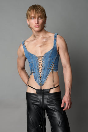 Model wearing blue washed denim corset top with plunging neckline, lace-up front and sides, raw frayed hem, and structured fit