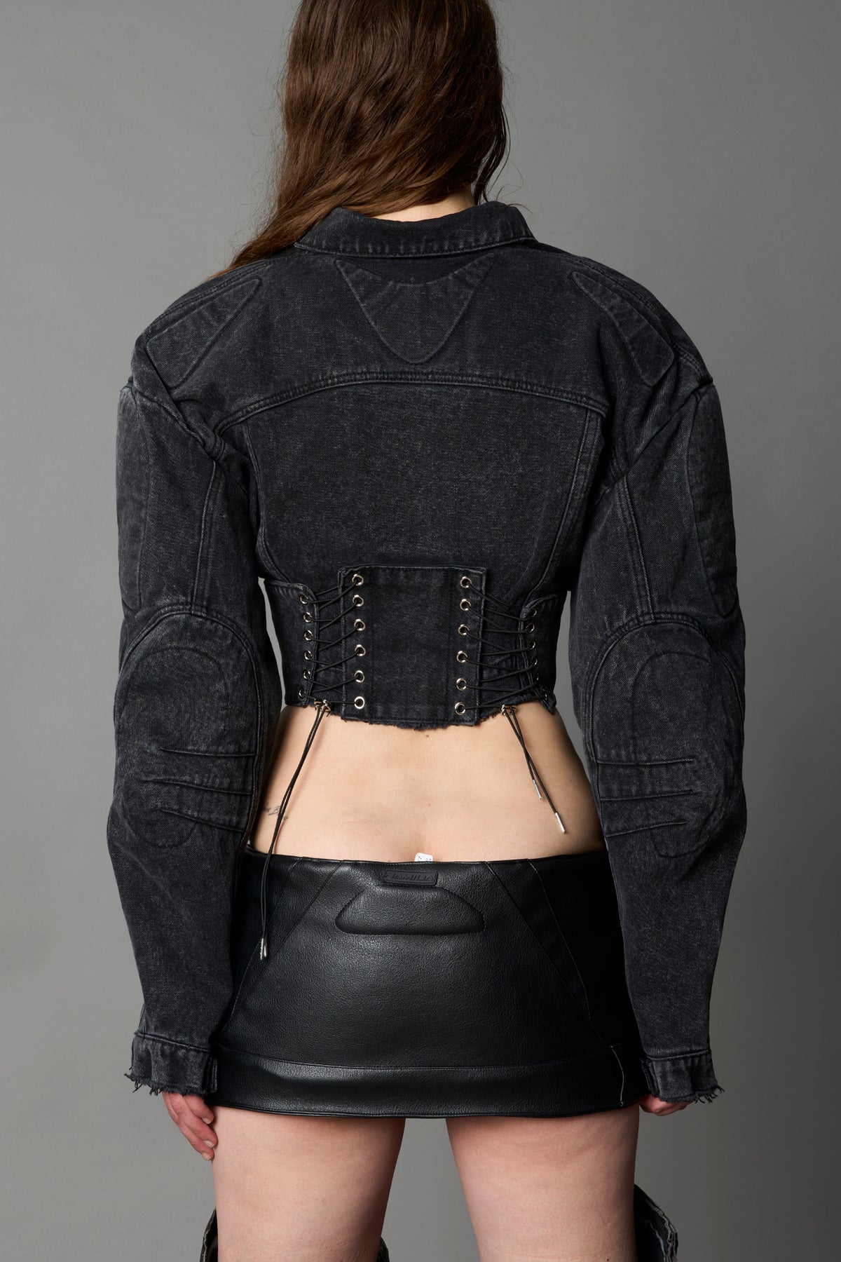 Back view of washed black denim corset jacket with lace-up detail, sculpted biker padding and cropped fit

