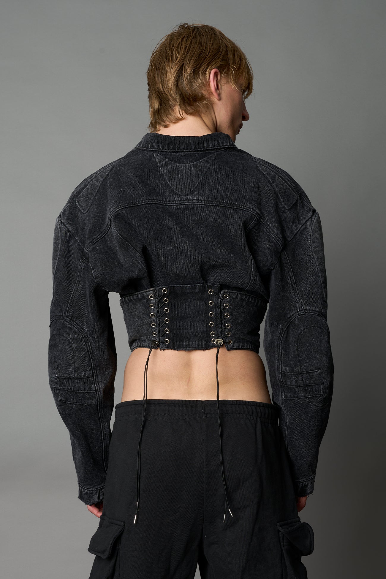 model wearing black washed denim jacket with structured corset waist and moto-style silhouette