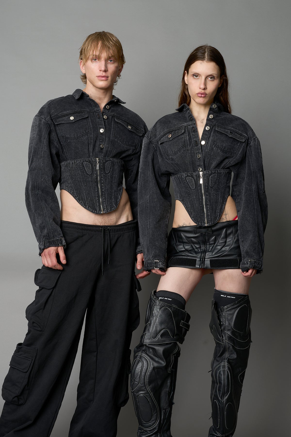 Front view of washed black denim jacket with structured corset waist and moto-style silhouette

