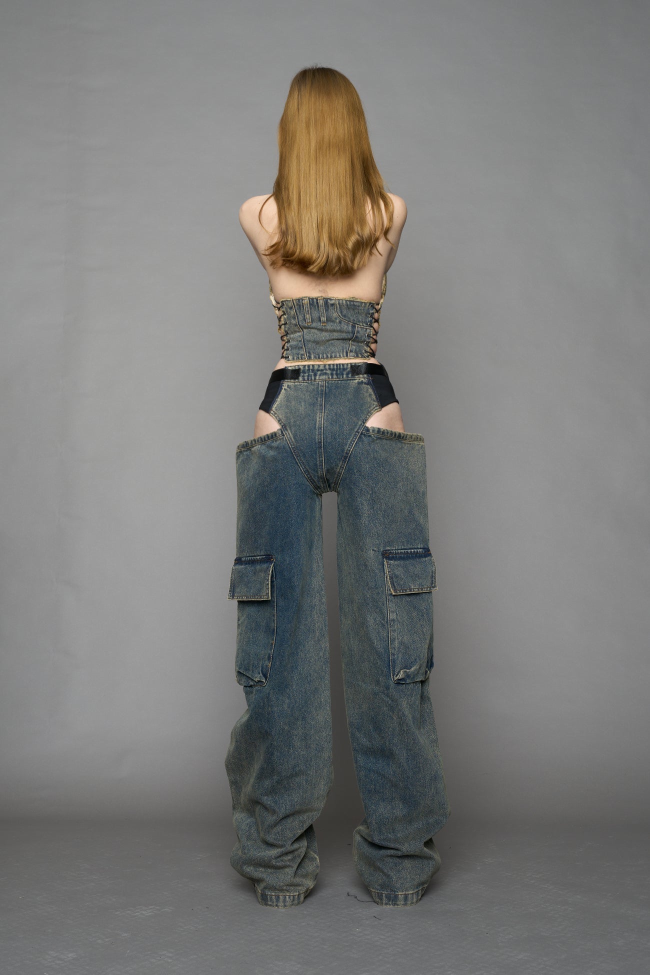 model wearing blue mud washed denim trousers with cut out design and 3D pockets