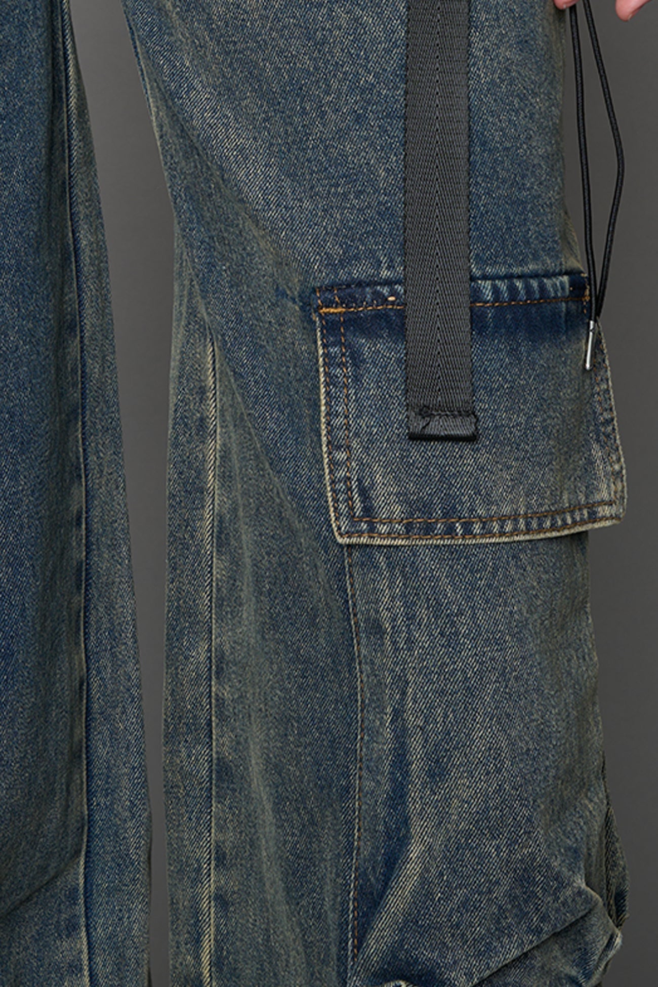 model wearing blue mud washed denim trousers with cut out design and 3D pockets
