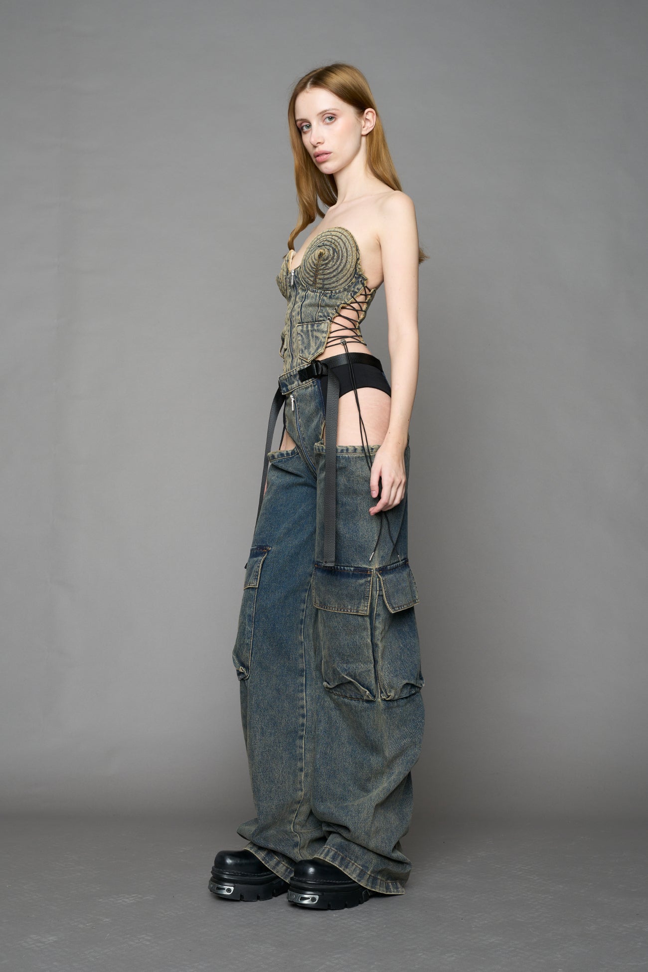 model wearing blue mud washed denim trousers with cut out design and 3D pockets