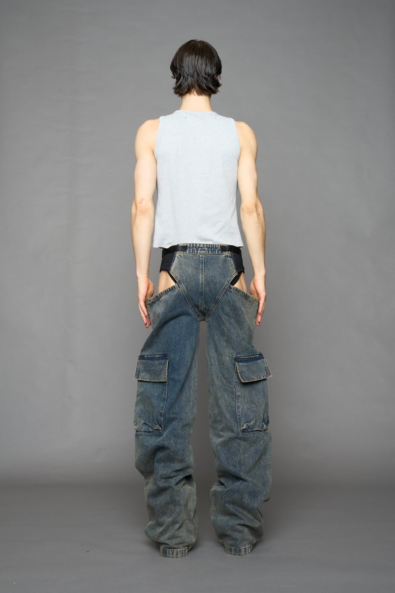 model wearing blue mud washed denim trousers with cut out design and 3D pockets